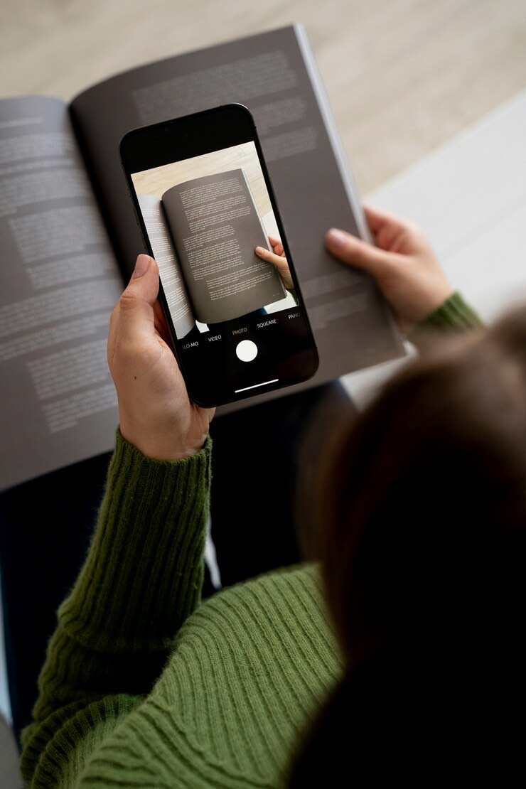 Una chica con u libro y que tiene un telefono e la mana para llamar a tu lector personal